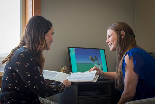 Two women engaging in a discussion while reviewing materials beside a computer.