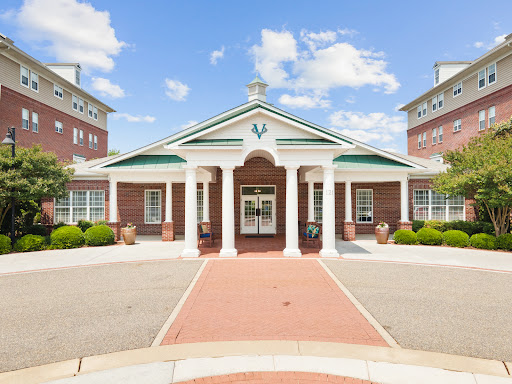 A welcoming entrance to a modern building, featuring classical columns and landscaped surroundings under a bright blue sky.