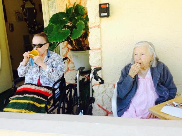 Two elderly individuals enjoying a drink and a snack outdoors on a sunny day.