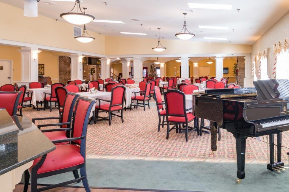 A spacious dining room with red chairs, white tablecloths, and a grand piano.