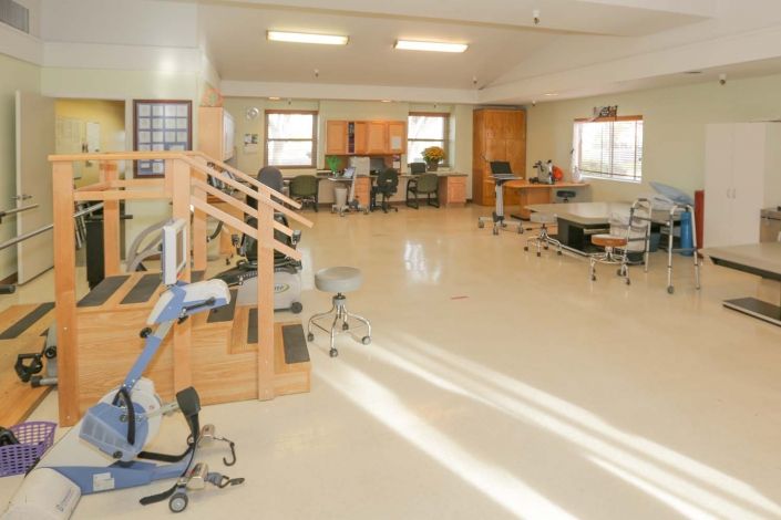 A bright physical therapy room equipped with various exercise machines and rehabilitation tools.