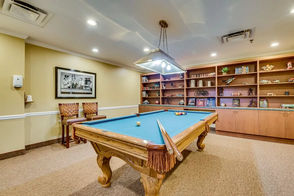 A cozy billiards room featuring a pool table, bookshelves, and warm lighting.