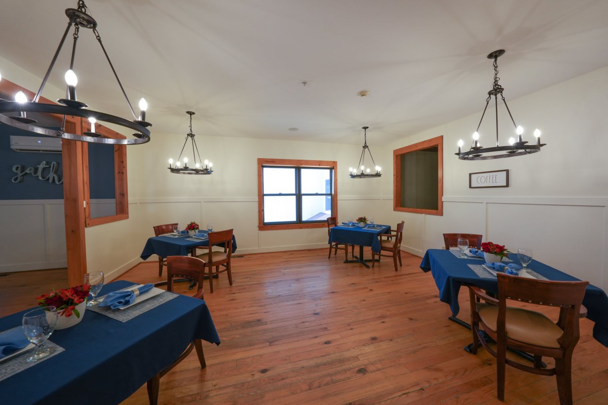 A cozy dining room with blue tablecloths, wooden floors, and elegant chandeliers.