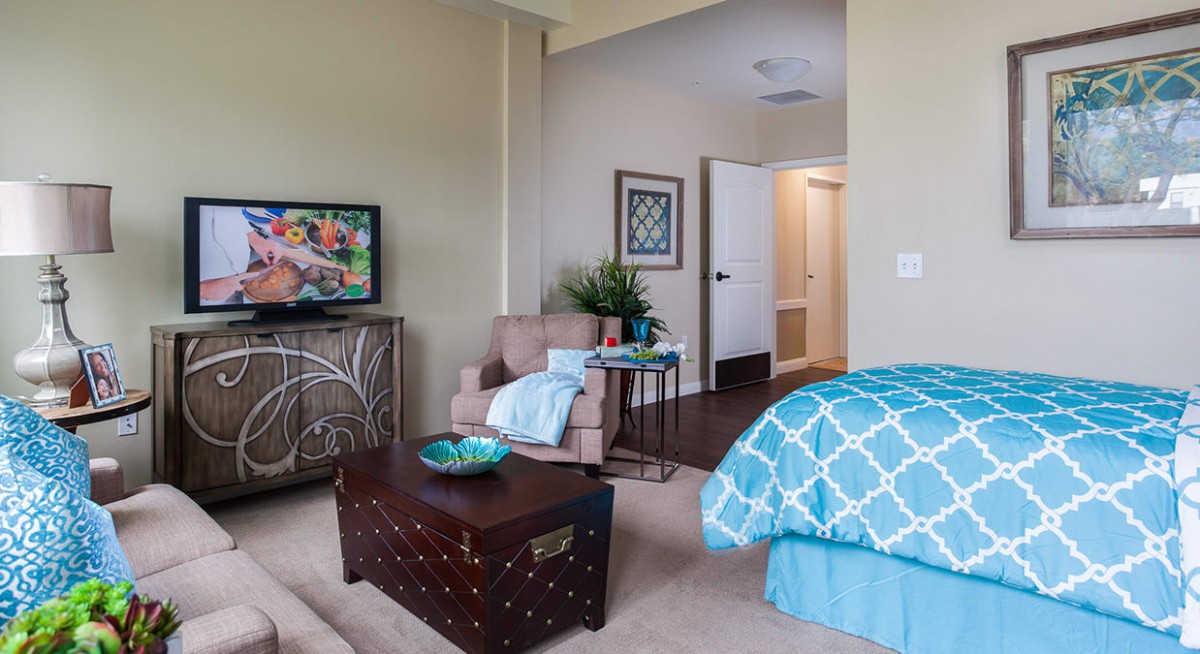 A cozy bedroom featuring a comfortable armchair, vibrant artwork, and a stylish blue bedspread.