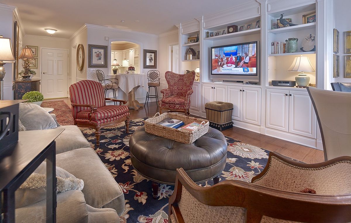 A cozy living room featuring comfortable seating, a patterned rug, a wall-mounted television, and built-in shelving.