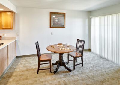 A minimalist dining area with a round table and two chairs on carpeted flooring, featuring a framed picture on the wall.