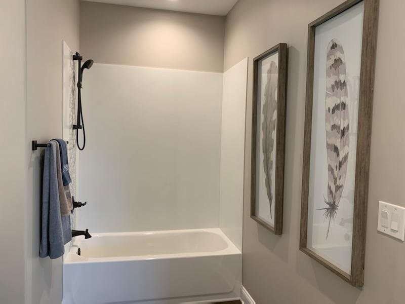 A modern bathroom featuring a bathtub with a shower, adorned with wall art and neatly hung towels.