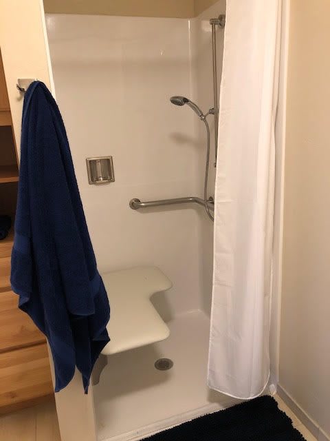 A bathroom shower with a blue towel hanging outside and safety grab bars installed inside.
