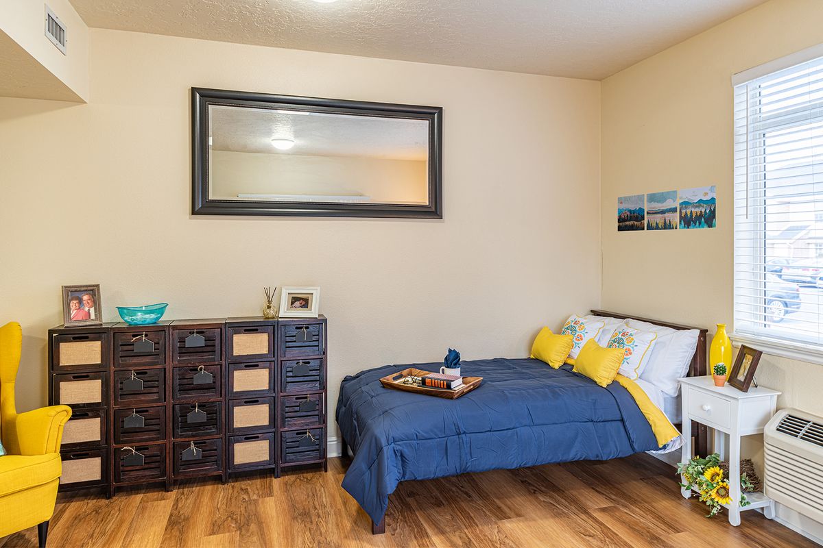 A cozy bedroom with a bed adorned in blue and yellow accents, featuring a large mirror above a wooden dresser.