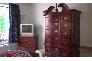A bedroom with a wooden armoire and a dresser topped with a television.