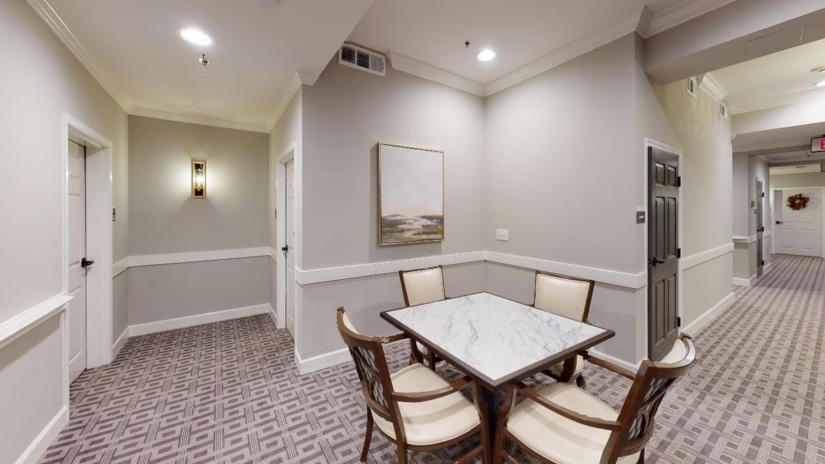 A small dining area with a marble-top table and four chairs, adorned with wall artwork and illuminated by ceiling lights.