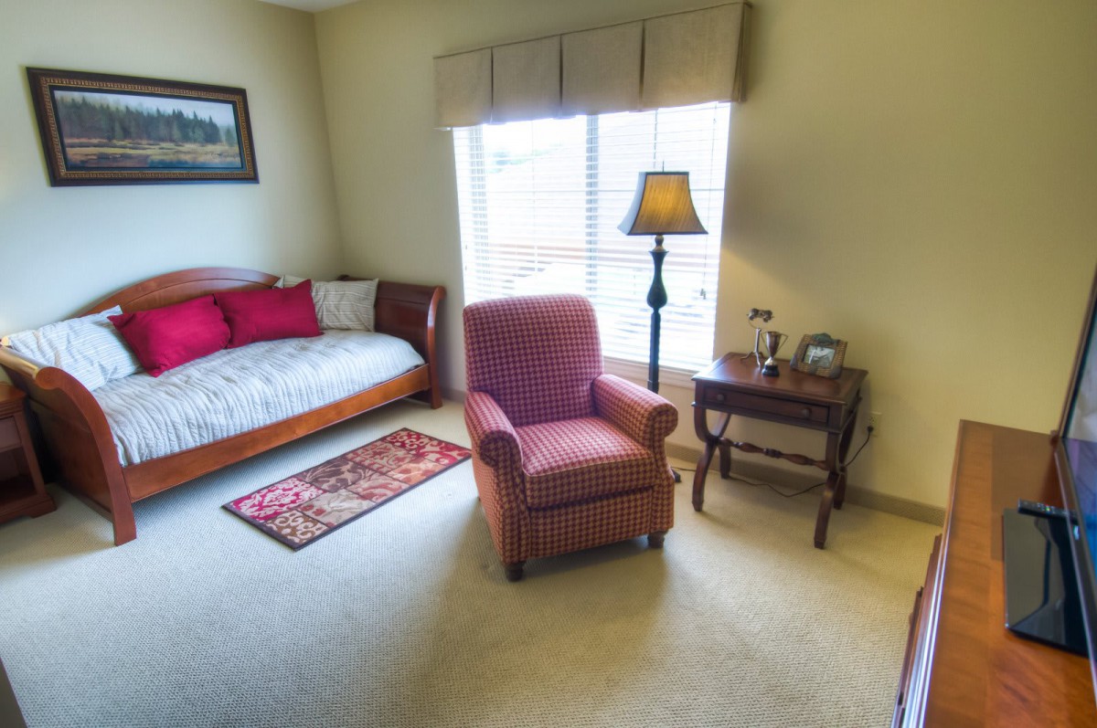 Cozy living room with an armchair, daybed, and lamp by the window.