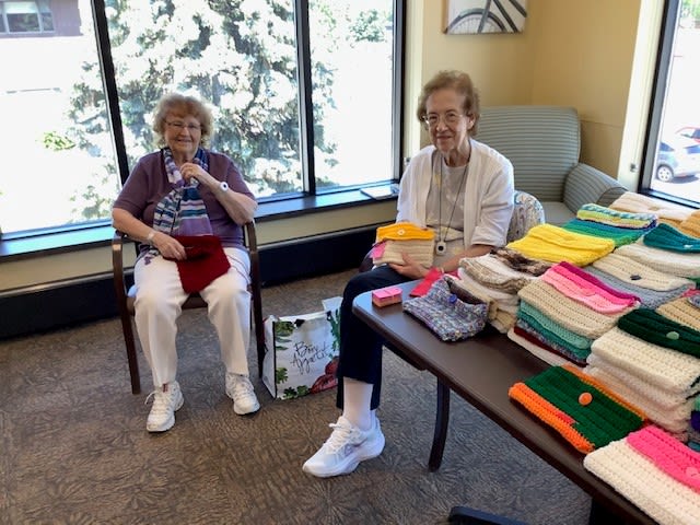 Two elderly women sitting indoors, enjoying a knitting session with colorful yarn.