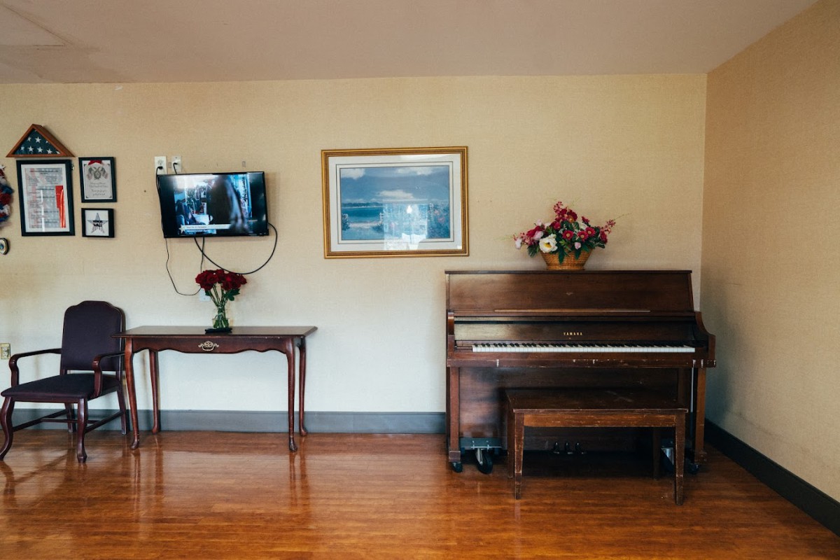 A cozy living room with a piano, wall-mounted television, and decorative flowers on a table.