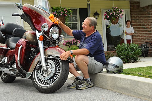 A man takes a moment to clean and maintain his motorcycle in front of a cozy home.