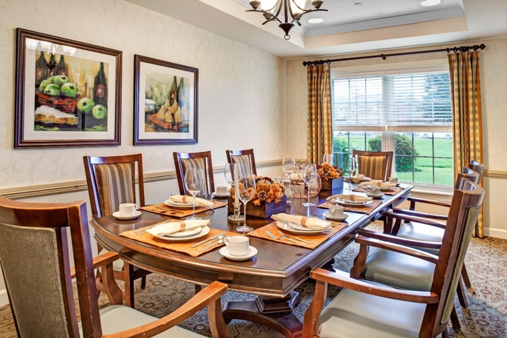 A well-decorated dining room with a large table set for a meal, featuring elegant chairs and artwork on the walls.