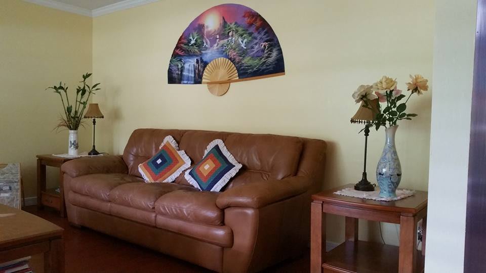 A cozy living room with a brown leather sofa, colorful decorative pillows, a stylish wall art piece, and a small lamp on a side table.