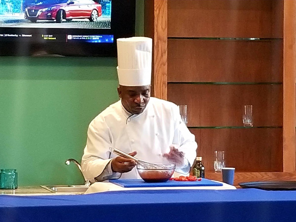A chef in a white uniform and tall hat preparing food during a cooking demonstration.