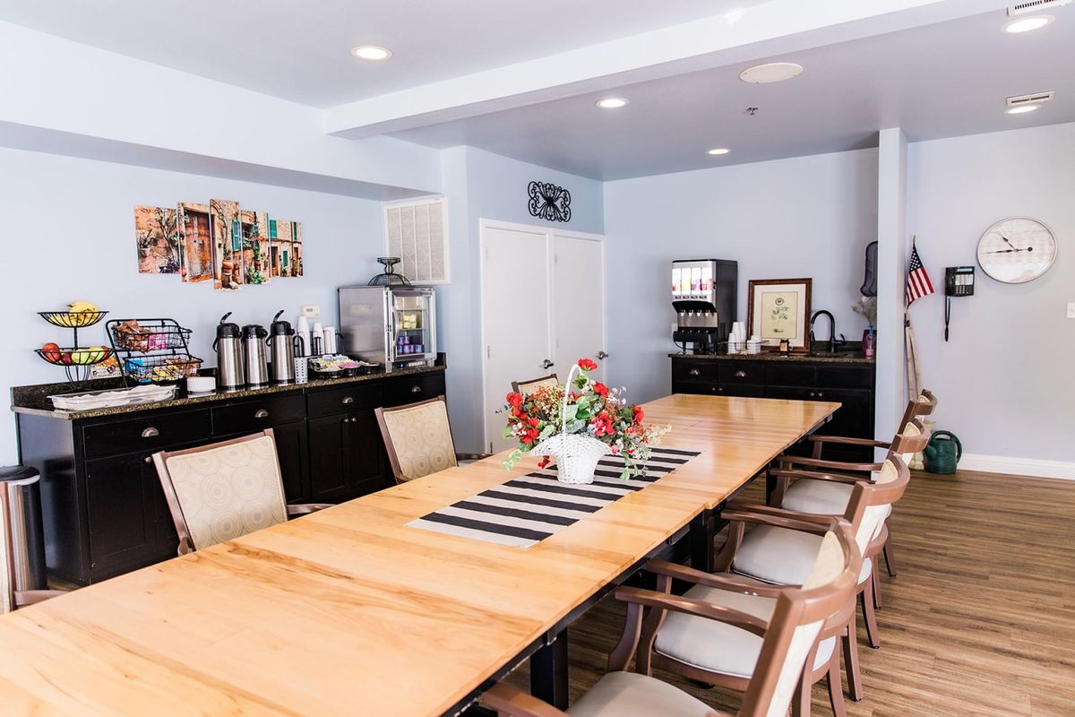 A modern conference room featuring a large wooden meeting table with chairs, a coffee station in the corner, and decorative flowers on the table.