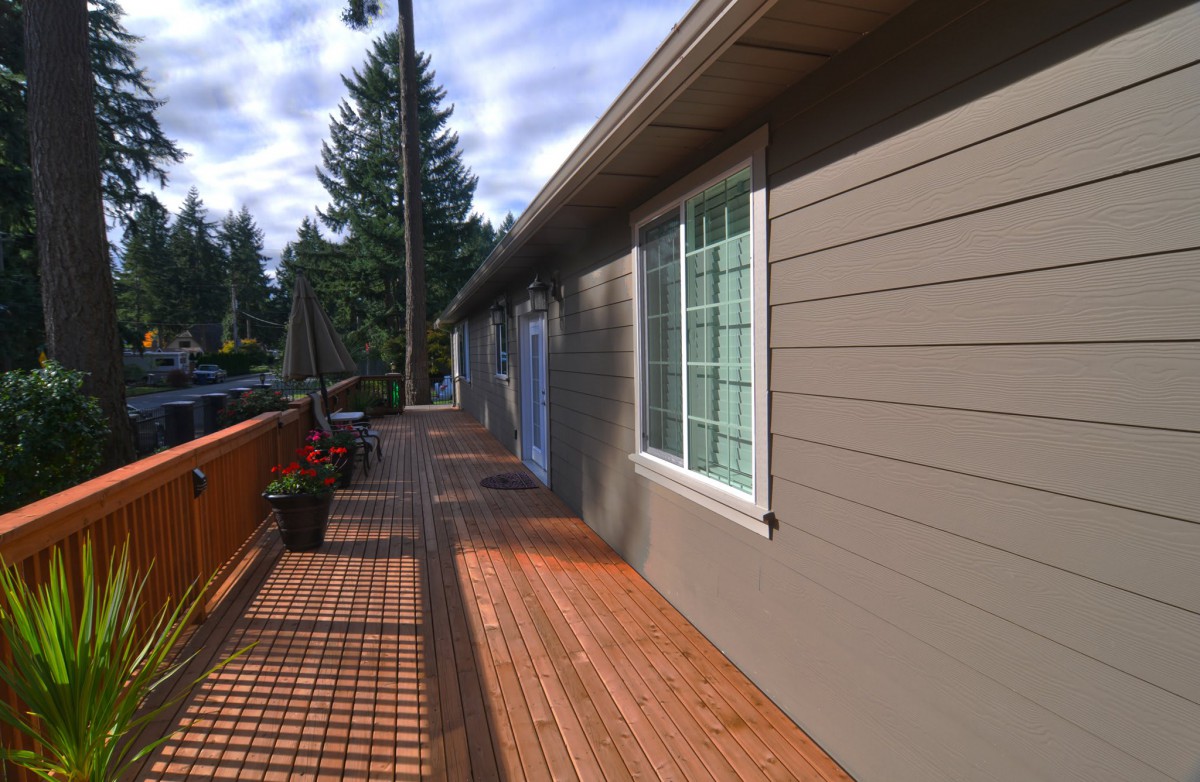 A wooden deck extending along the side of a house on a sunny day.