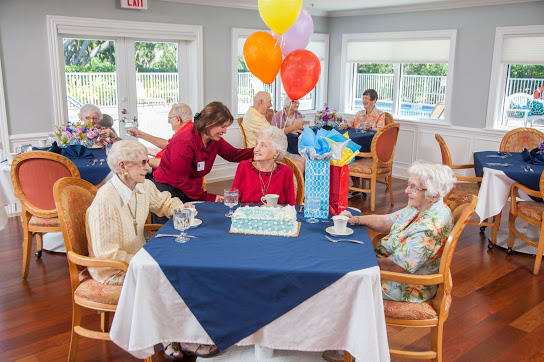A group of seniors celebrating a birthday with cake and balloons in a cozy room.