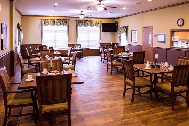An empty restaurant dining area with neatly arranged tables and wooden flooring.