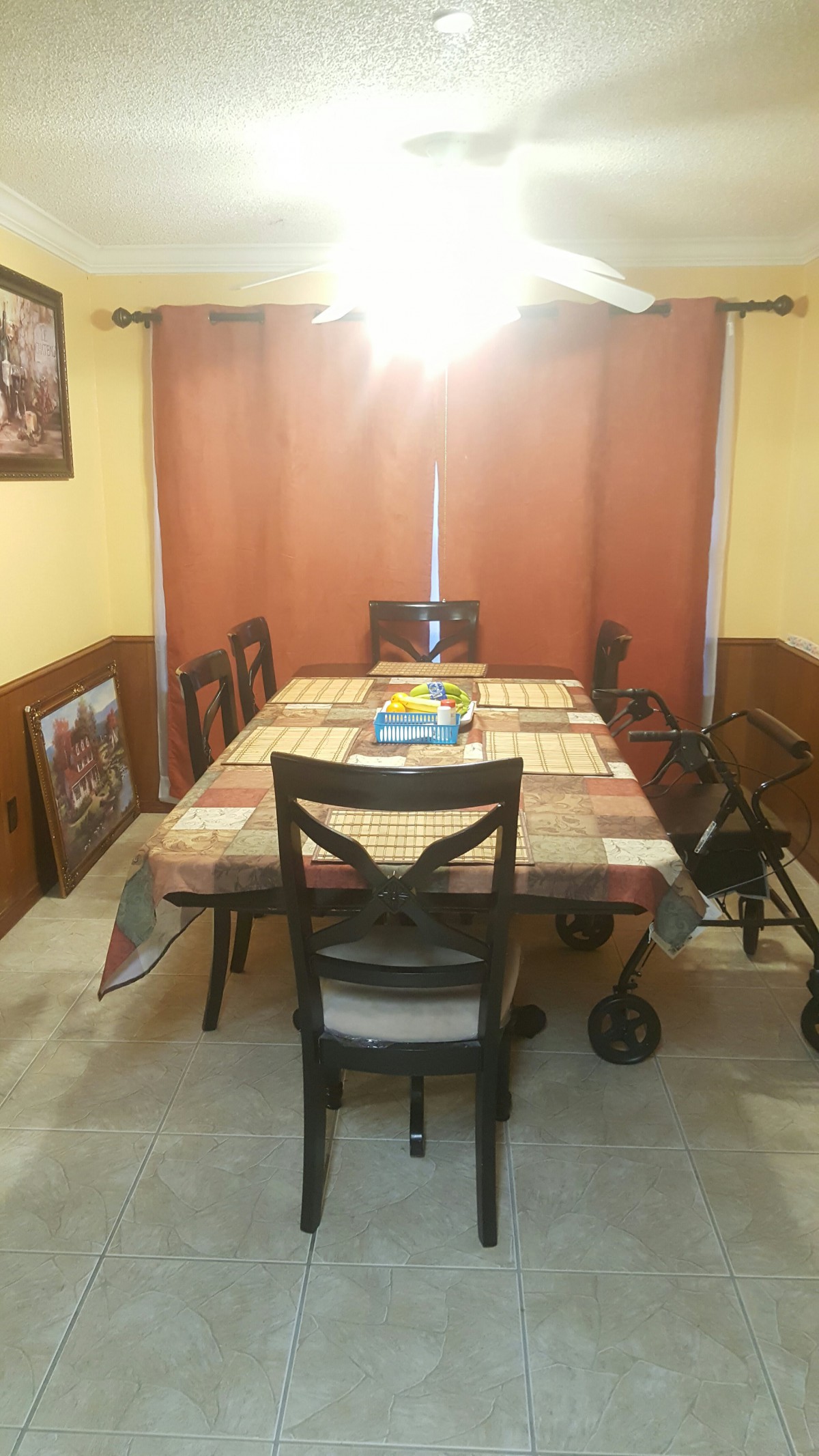 A dining room with a table and chairs, featuring a colorful tablecloth and a walker nearby.