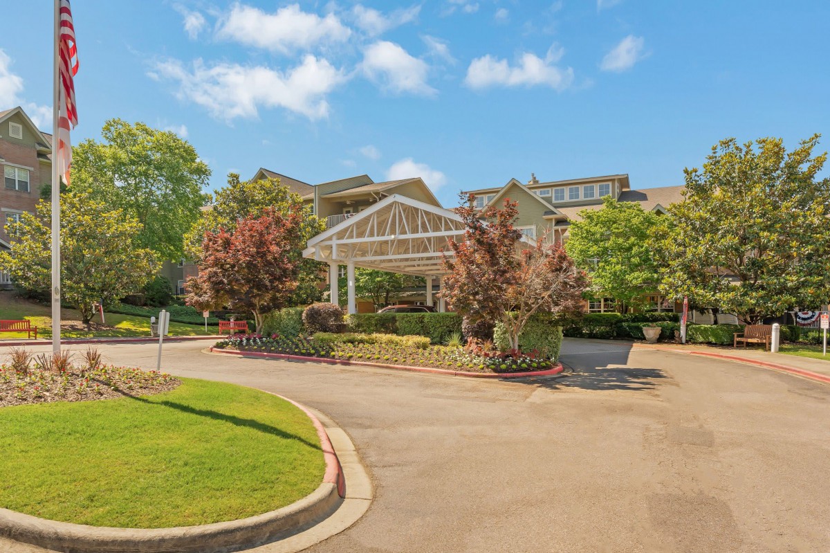 A scenic view of a building with a covered entrance, surrounded by trees and a clear blue sky.