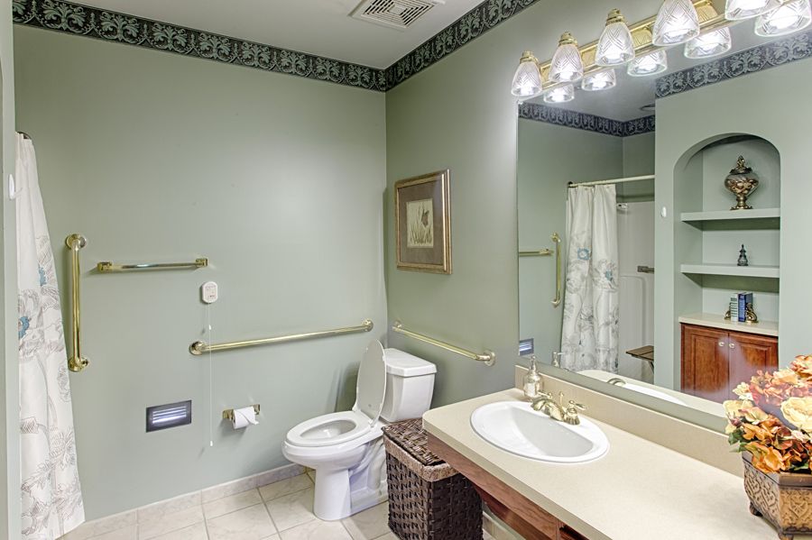 A spacious bathroom with a toilet, sink, and large mirror, well-lit by overhead lights.
