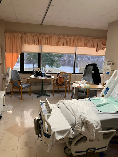 A view of a hospital patient room featuring a bed, chairs, and medical equipment.