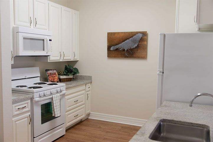 A modern kitchen with white cabinets and appliances, featuring a stove, microwave, and a piece of artwork on the wall.