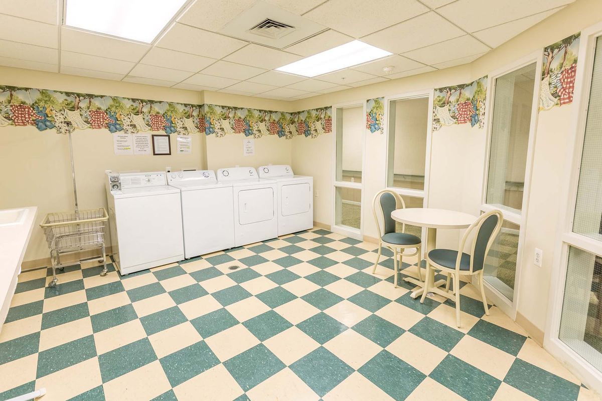 A laundry room with washing machines, a checkered floor, and a small table with chairs.