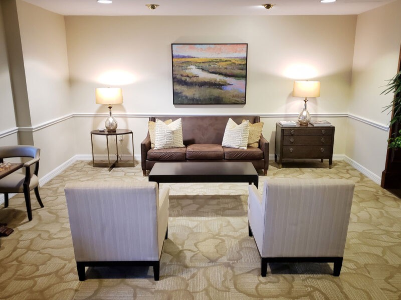 A cozy living room setup with a sofa, two chairs, and a coffee table, complemented by art on the wall and warm lighting from lamps.