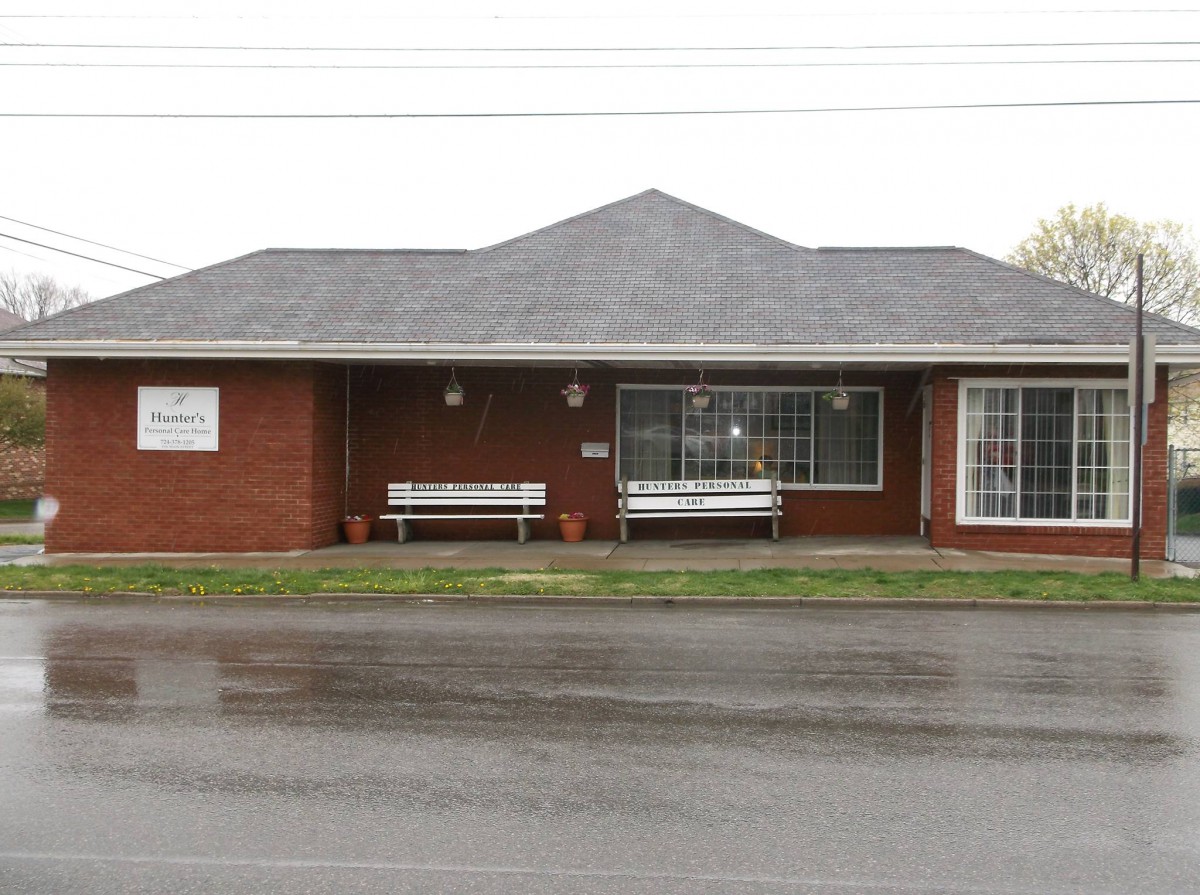 A small brick building with large windows and benches outside on a rainy street.