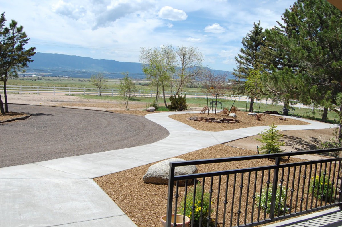 A scenic outdoor landscape with a pathway, trees, and distant mountains under a partly cloudy sky.