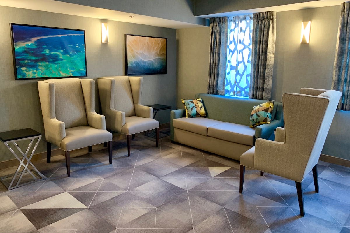 A cozy living room featuring elegant chairs and a sofa, complemented by artistic wall paintings and decorative curtains.