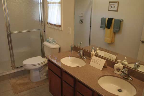 A bathroom featuring a double sink vanity with mirrors, a toilet, and a shower.