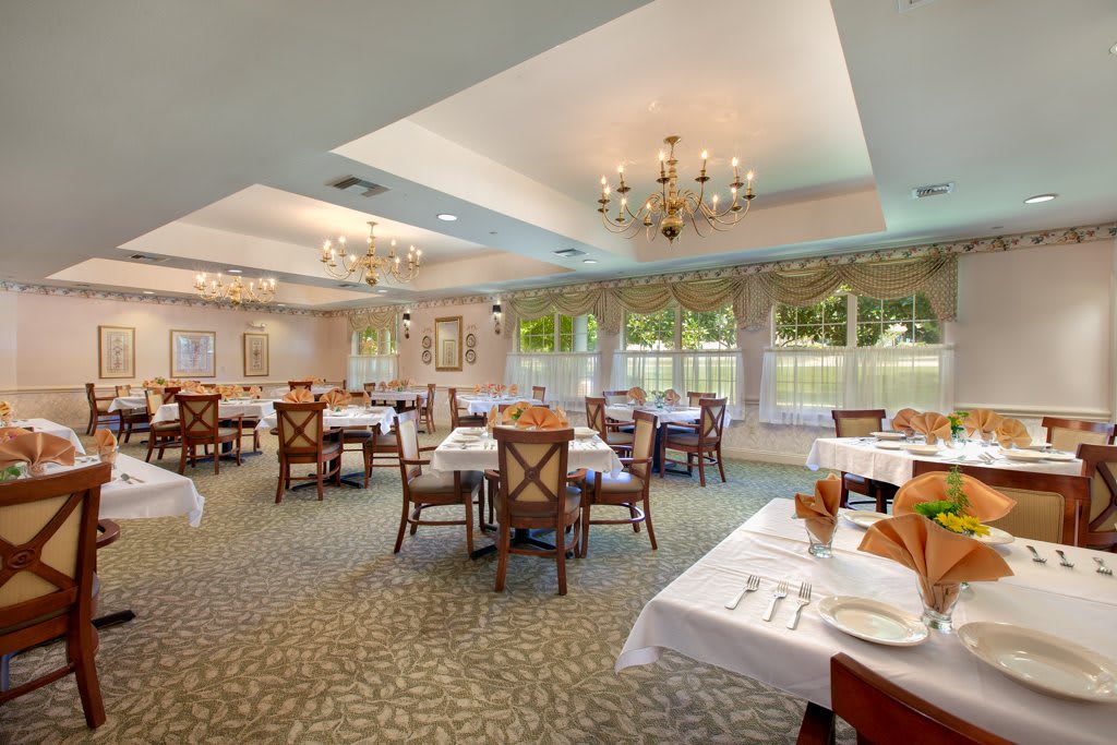 An elegant dining room with chandeliers and set tables, offering a scenic window view.