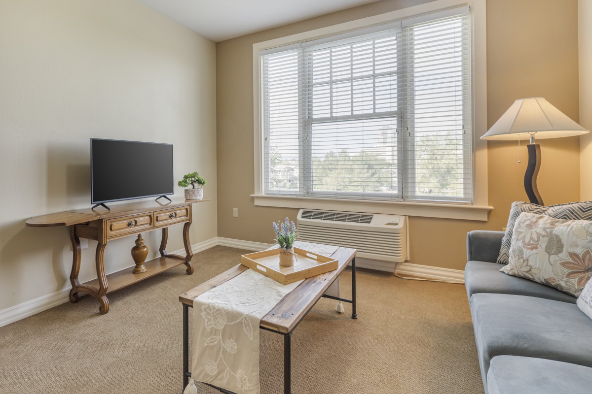A cozy living room with a television, coffee table, and large window allowing natural light.