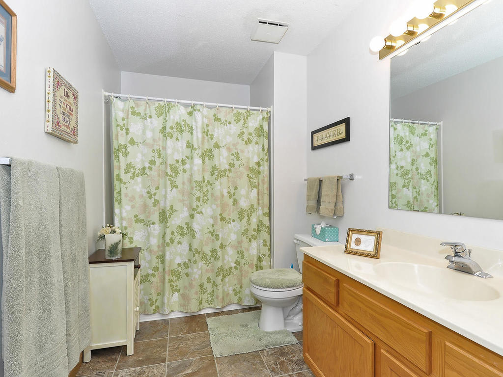 A well-lit bathroom featuring a floral shower curtain, vanity with sink, and wall decor.
