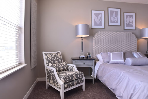 A cozy and elegantly designed bedroom featuring a patterned chair, stylish lamp, and a neatly made bed.
