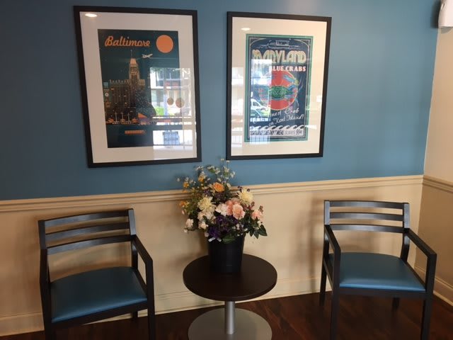 A cozy waiting area with two chairs, a table with a flower arrangement, and framed posters on the wall.