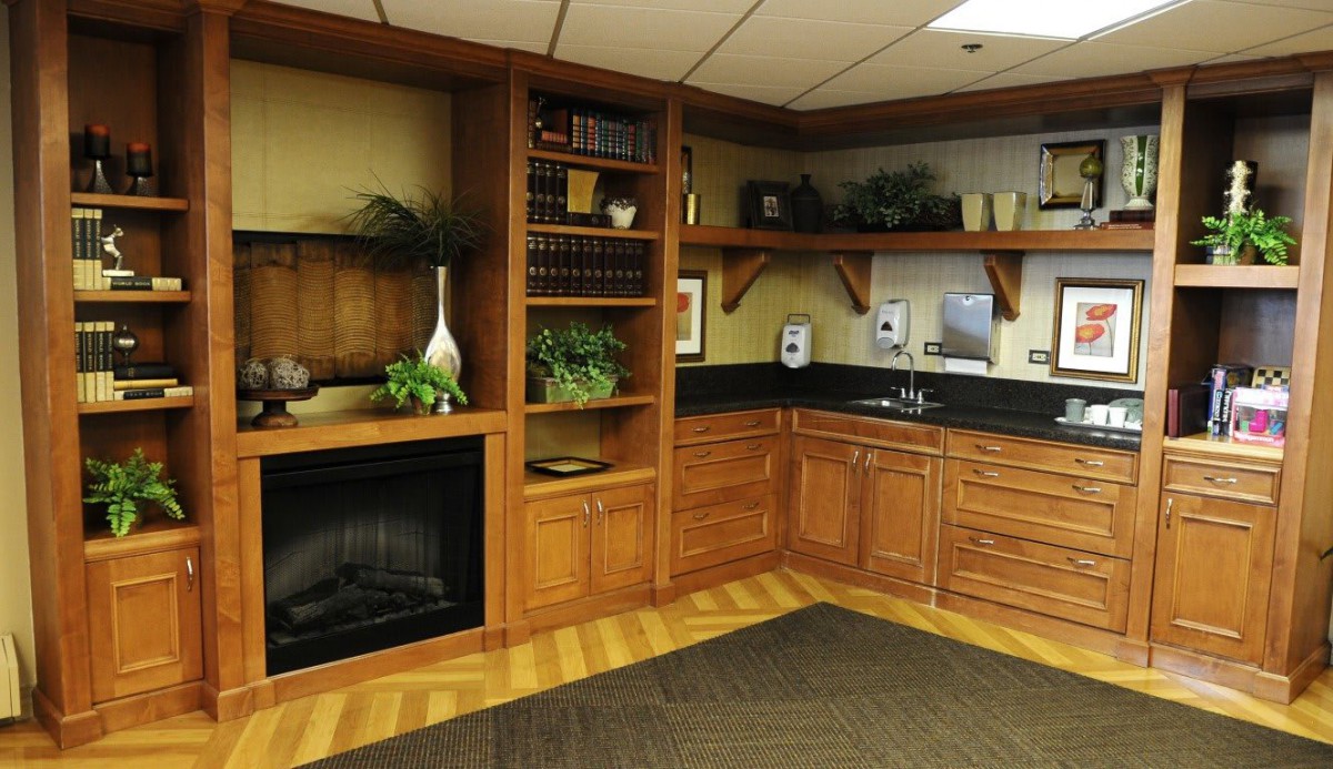 A cozy office corner featuring a wooden bookshelf, built-in fireplace, and cabinetry with a small sink.