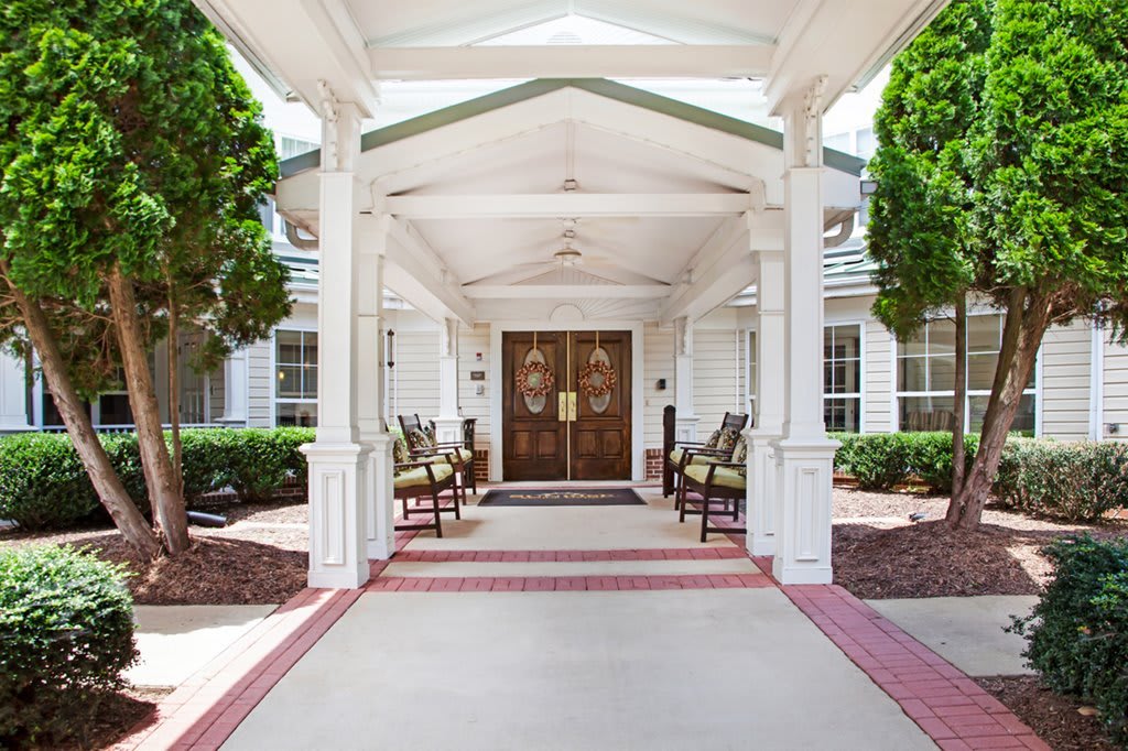The entrance of a building with a covered porch and two chairs flanking the doorway.