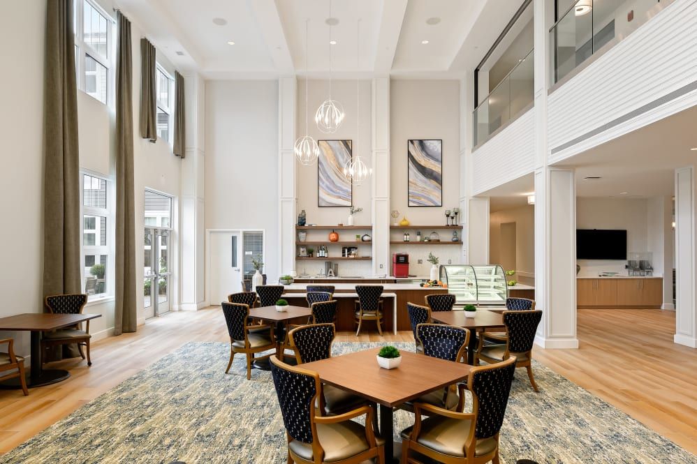 A modern dining space with high ceilings, featuring elegant tables and chairs, large windows, and decorative artwork.