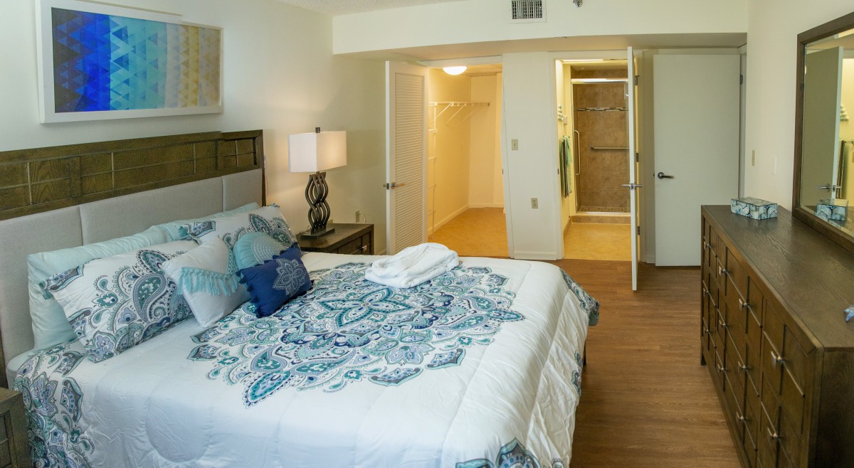 A cozy bedroom with a neatly made bed, decorative pillows, and an open door leading to a walk-in closet.