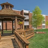 A wooden gazebo in front of a brick building on a sunny day.