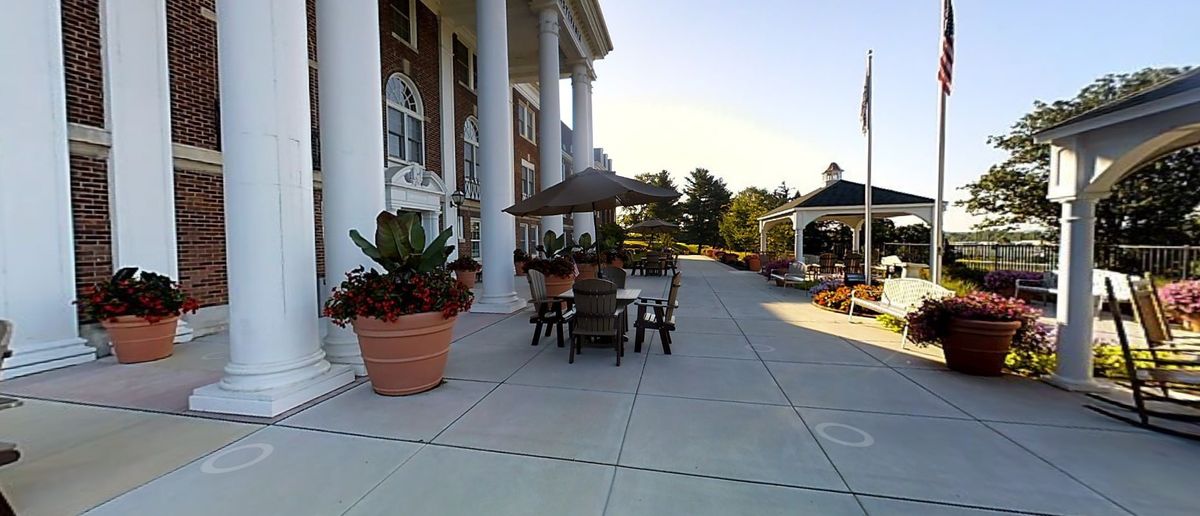 An elegant outdoor patio area with large columns, furniture, and potted plants.