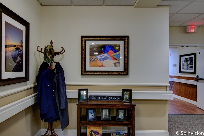 An office interior featuring a coat rack, a framed painting, and a bookshelf with photographs.