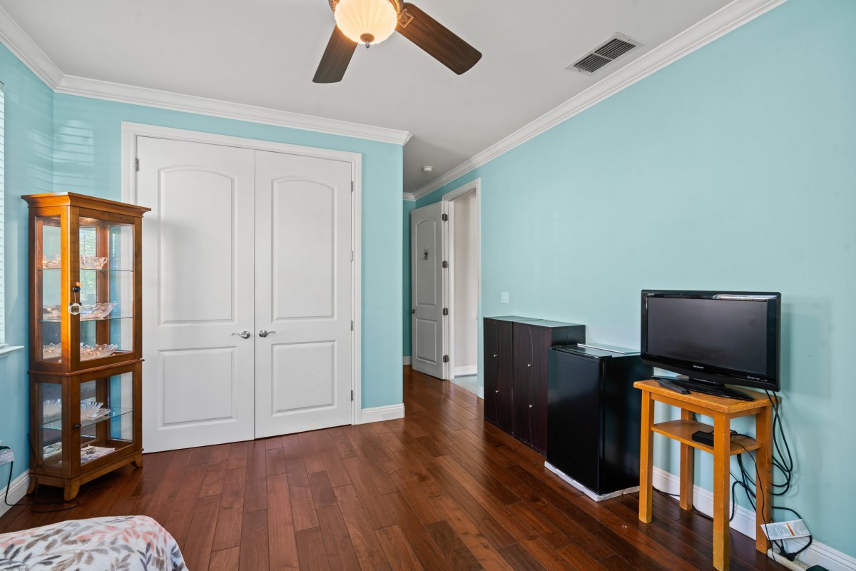 A cozy bedroom with blue walls, wooden flooring, and a ceiling fan features a closet and a small desk with a computer.